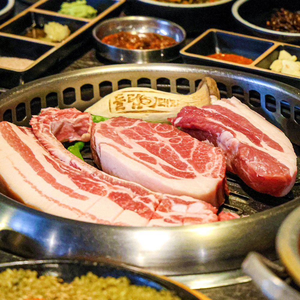 돌담흑돼지 중문점 — 둥근 불판 위에 올린 두툼한 흑돼지 오겹살과 목살, 둘레에 반찬 그릇