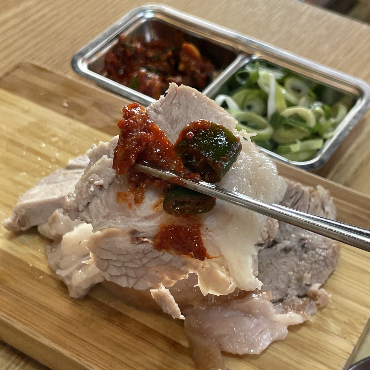 수육(돔베고기) — 나무 도마 위의 돼지고기 수육을 양념과 함께 집어 든 모습
