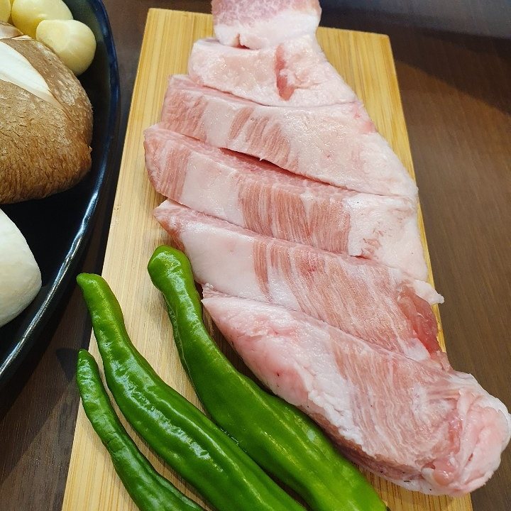 나무 도마에 올린 두툼한 흑돼지 생고기와 풋고추