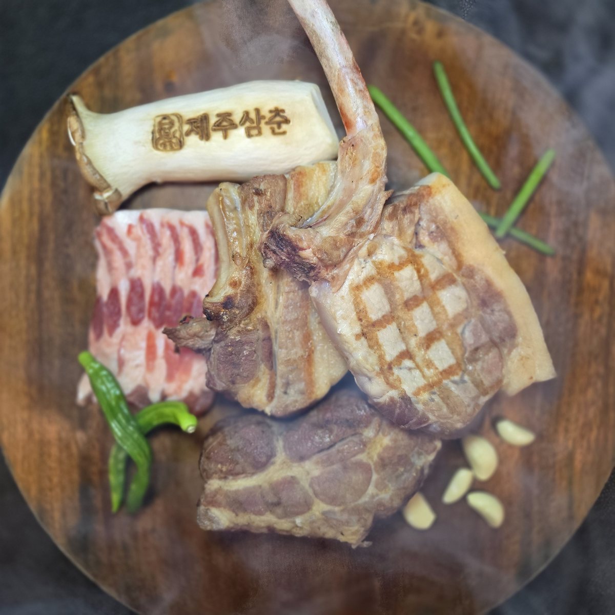 삼춘세트 — 둥근 나무판에 뼈 붙은 흑돼지와 오겹살·목살을 새송이버섯·풋고추와 담은 모습
