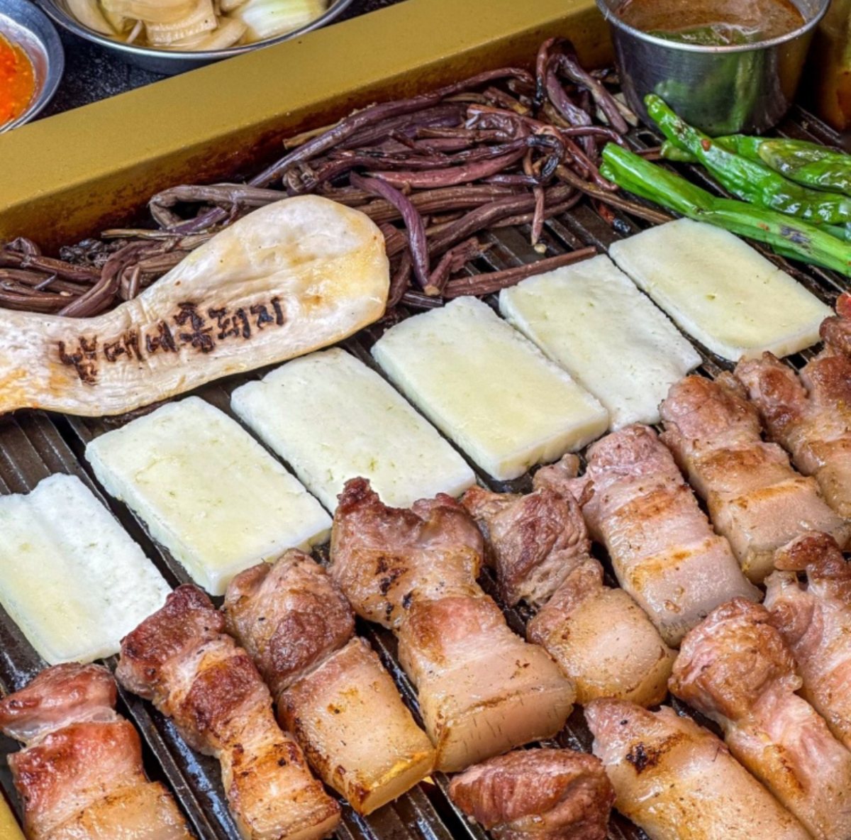 불판 위에서 노릇하게 익어 가는 흑돼지와 구운 치즈·고사리
