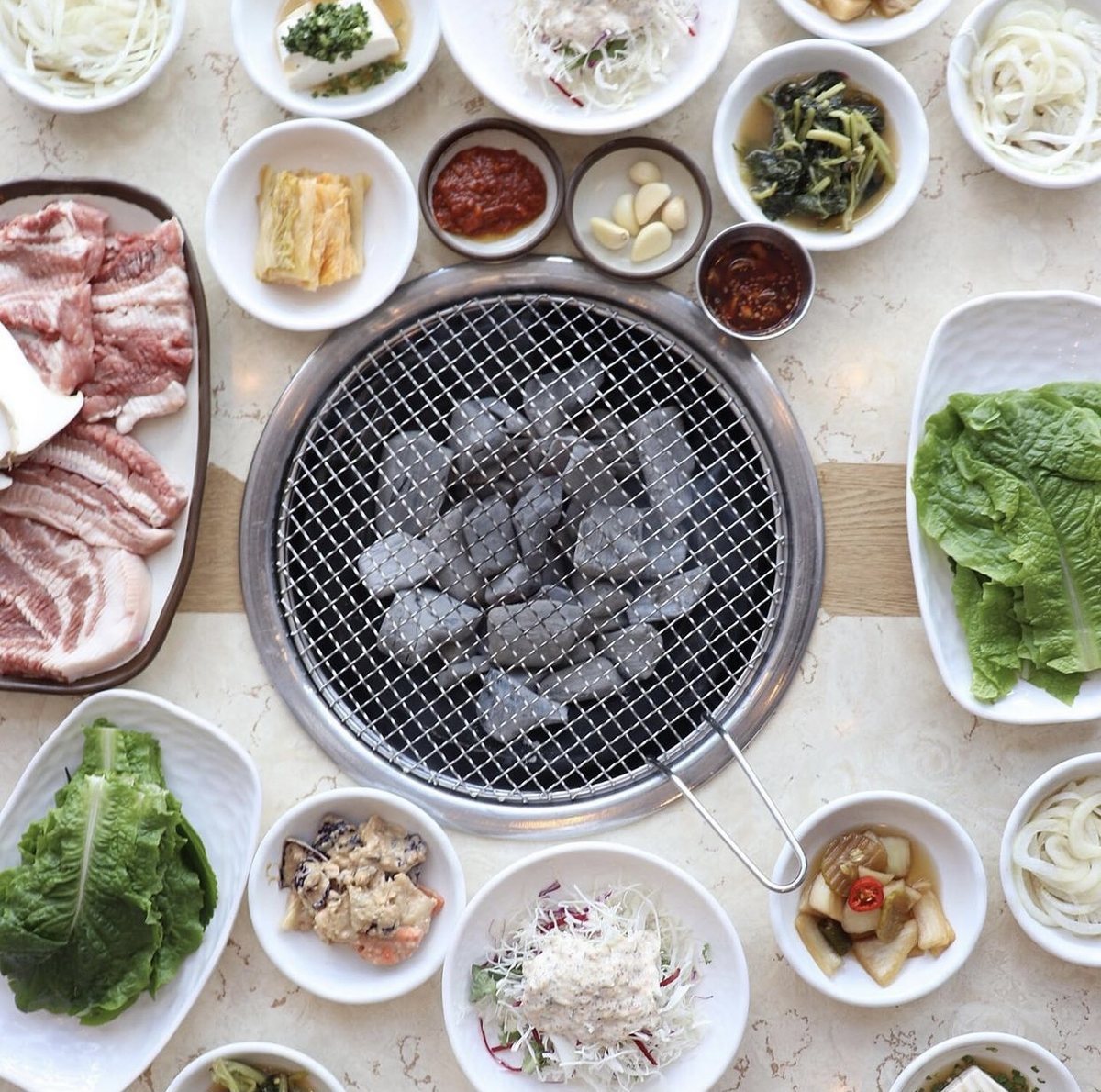 숯불 석쇠를 가운데 두고 생고기와 반찬·쌈 채소를 차린 상