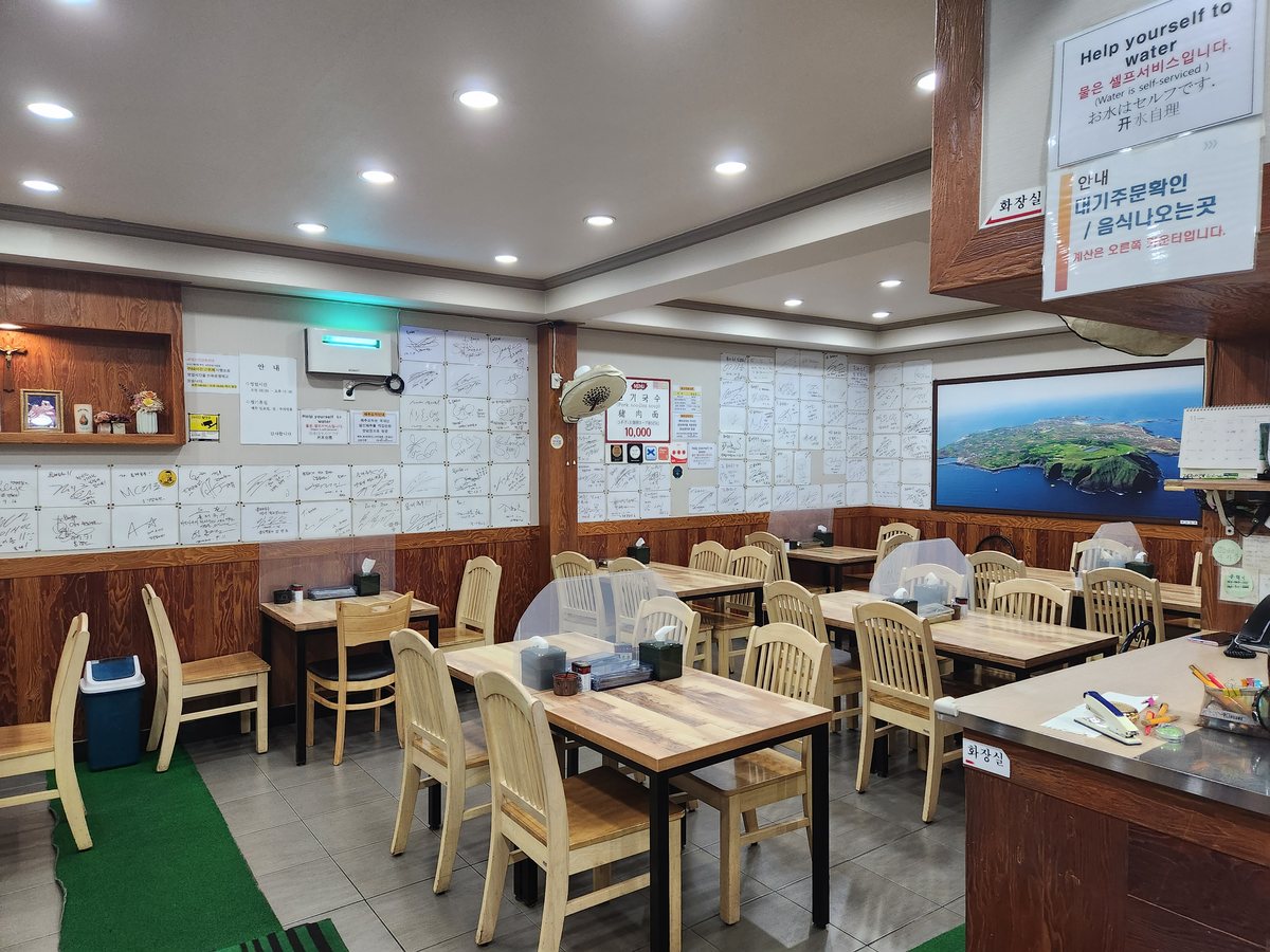 나무 의자와 식탁이 놓인 실내, 벽에 붙은 손님 사인