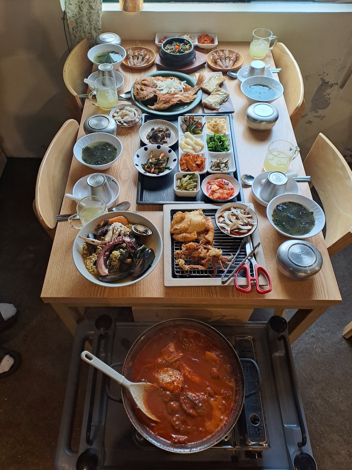 창가 식탁에 갈치조림 냄비와 여러 반찬을 차린 한 상